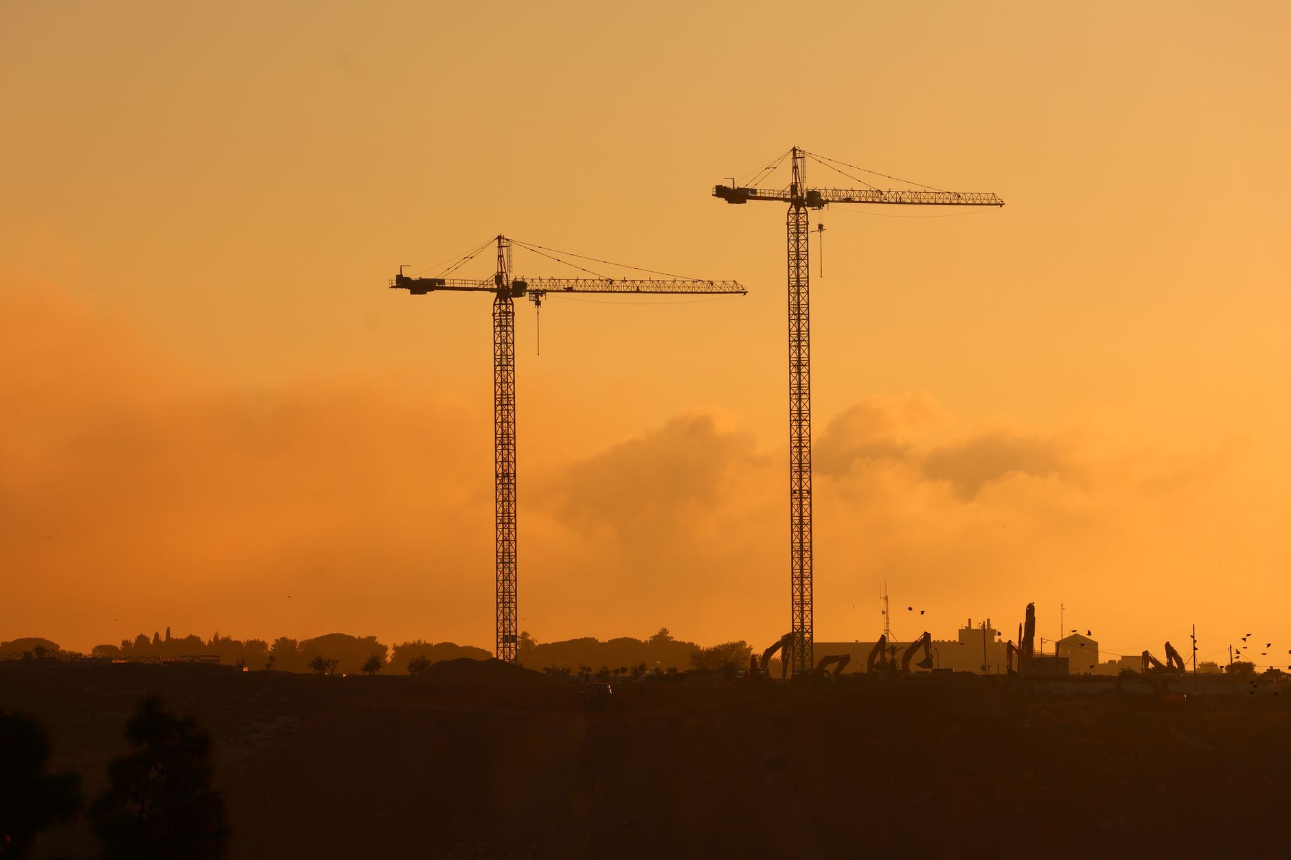 Silhouette of tall construction cranes against a vivid sunset sky, capturing urban development.
