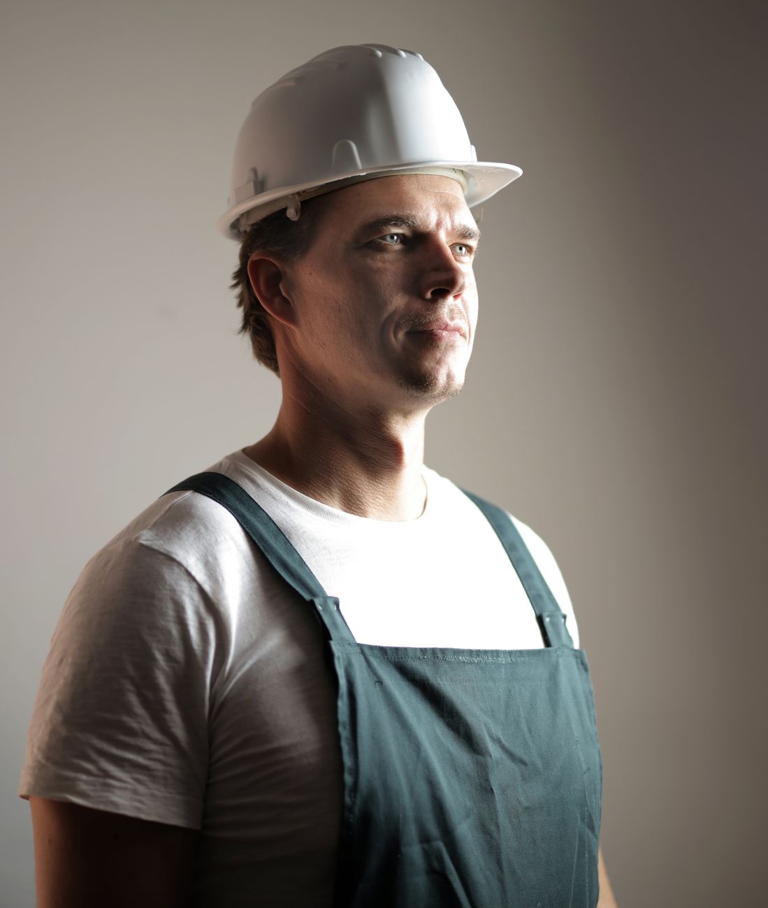Portrait of a confident construction worker in a hard hat, looking forward in studio lighting.